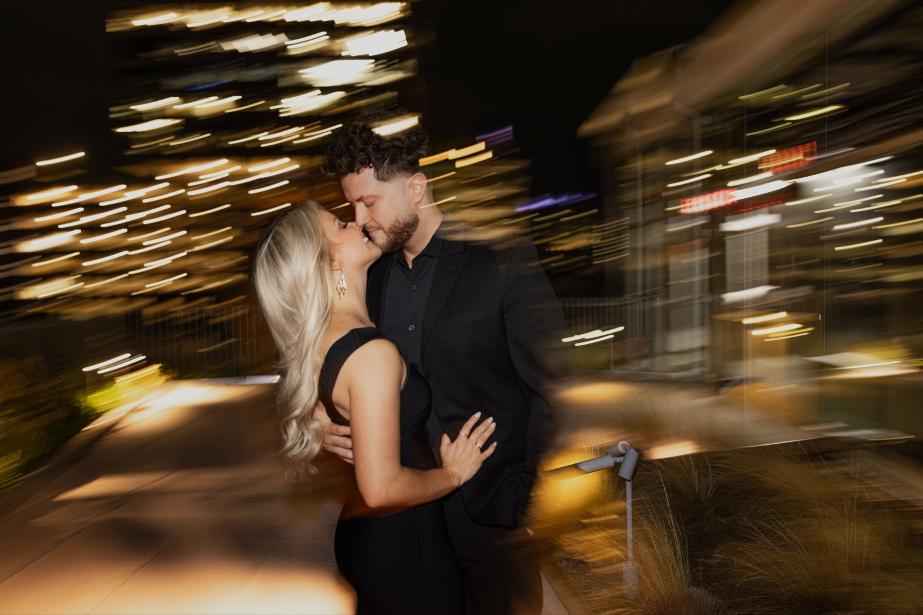 Phil and Sarah kissing at night, city lights streaking behind them.