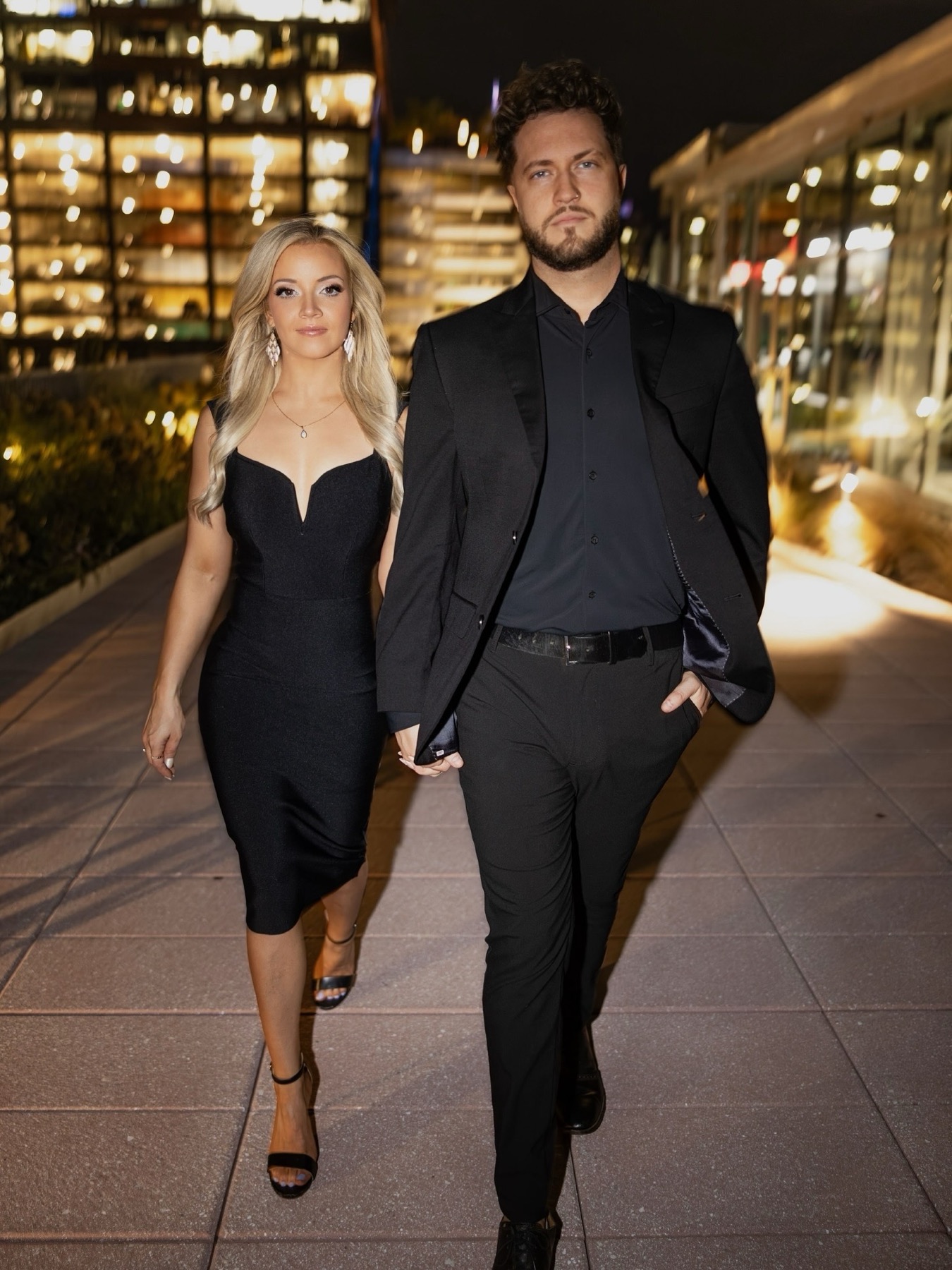 Phil and Sarah walking dressed in black, the skyline glowing behind them.