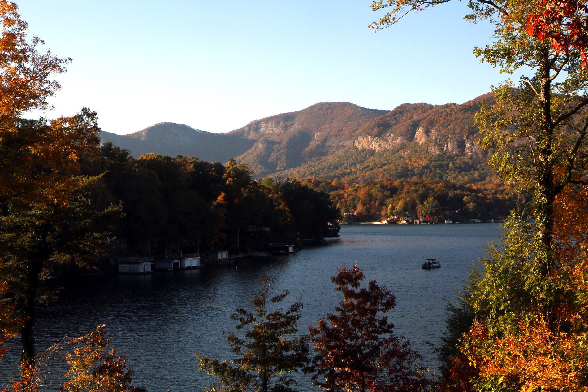 Lake Lure at peak fall color, boathouses along the shore and the gorge glowing behind.